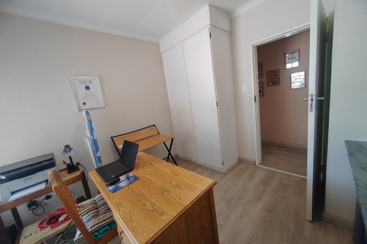A functional bedroom featuring built-in cupboards and light wood-look flooring, currently utilized as a home office space.