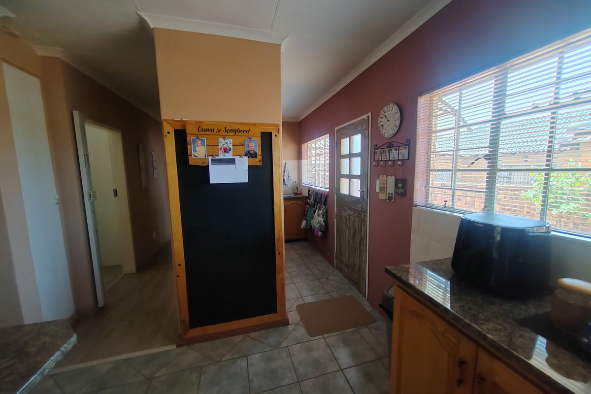 A functional kitchen area featuring tiled flooring, wooden cabinetry, and a built-in chalkboard partition, providing access to the home's interior hallway.