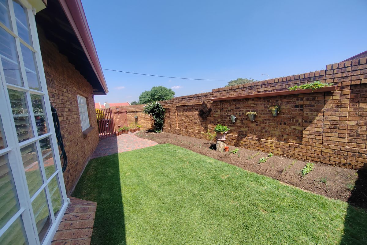 A well-maintained rear garden featuring a brick boundary wall, paved walkway, and a neat lawn area adjacent to the house exterior.