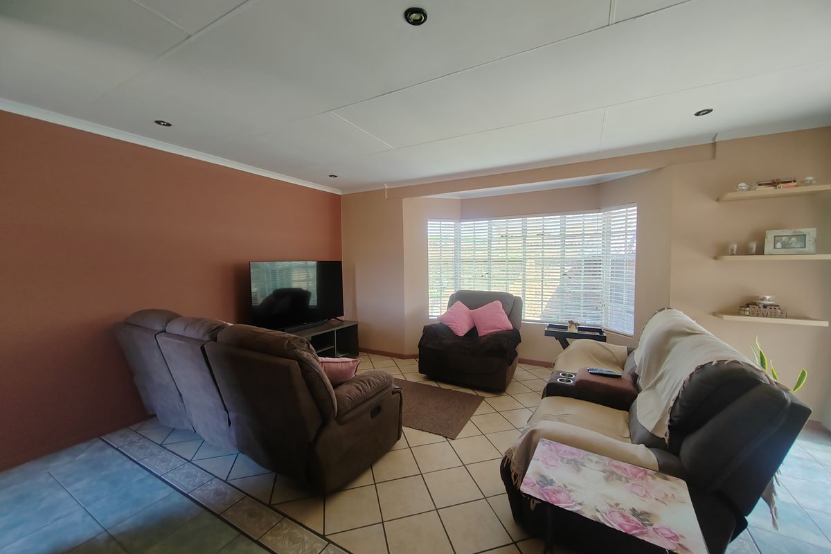 A comfortable living room featuring a large bay window with fitted blinds, tiled flooring, and recessed ceiling lighting.