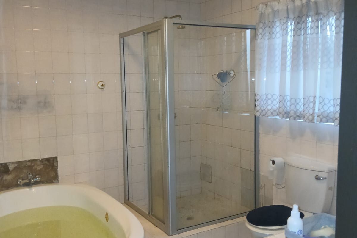 A functional bathroom featuring a built-in bathtub, separate glass-enclosed shower, and tiled finishes with exposed timber ceiling beams.