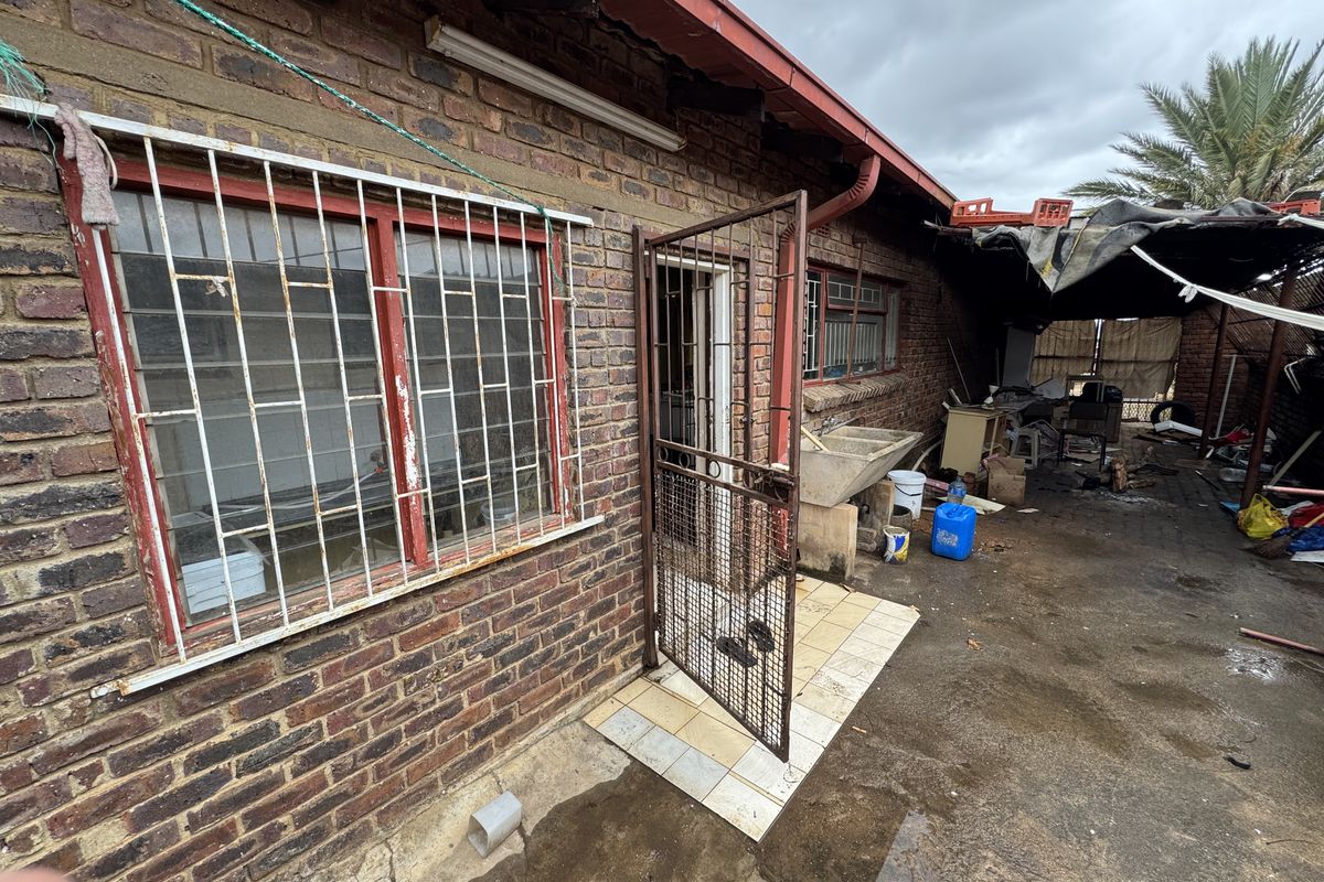 Rear exterior view of the property featuring a brick facade, security gates, and a concrete wash basin area requiring maintenance and structural improvements.