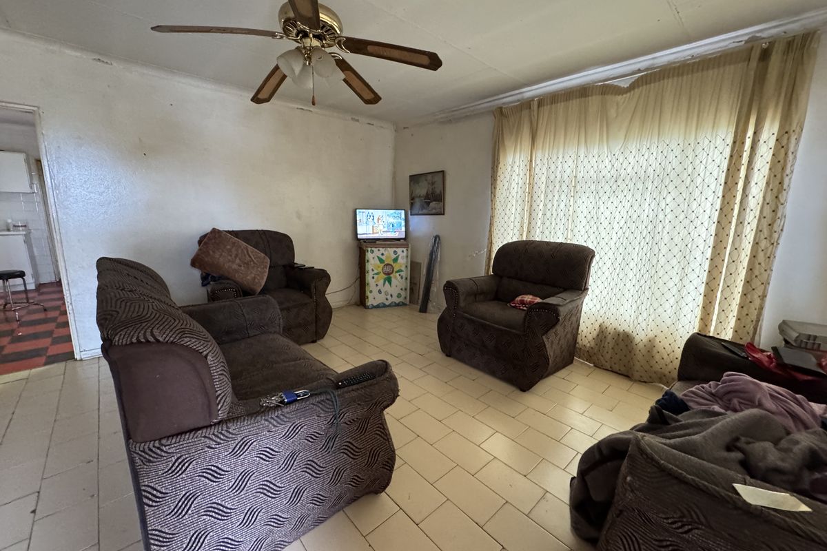 A living room featuring tiled flooring and a ceiling fan, requiring cosmetic updates to the walls and ceiling to improve the overall aesthetic.