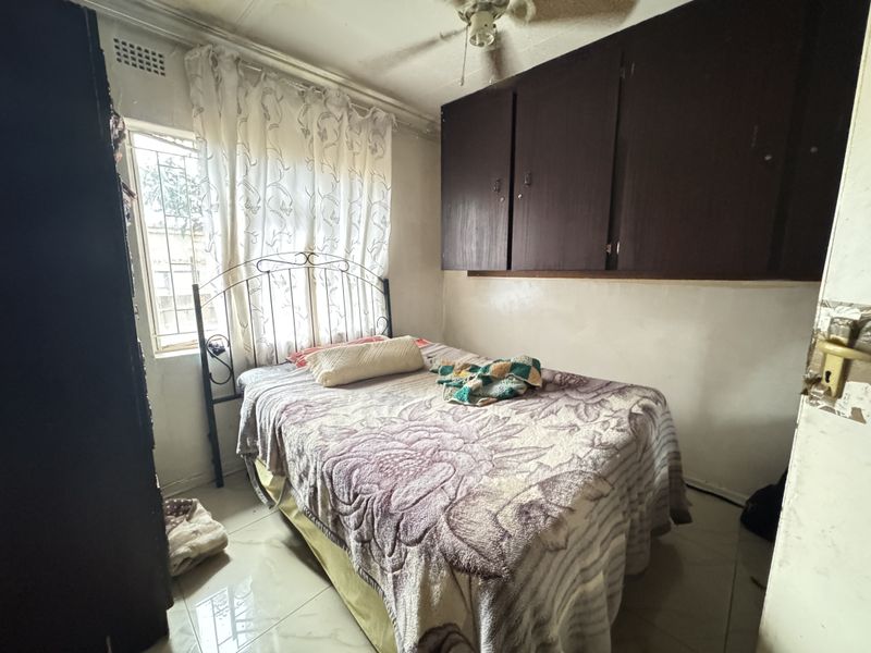 A compact bedroom featuring tiled flooring, built-in storage cupboards, and a ceiling fan, requiring cosmetic updates to improve its overall condition.