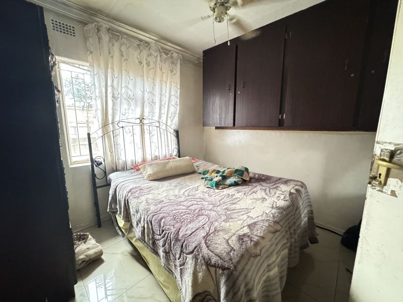 A compact bedroom featuring built-in cupboards and tiled flooring, requiring cosmetic updates to improve its overall condition and appeal.