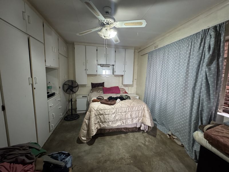 A bedroom featuring extensive built-in cabinetry and a ceiling fan, requiring cosmetic updates to the flooring and wall finishes to modernize the space.