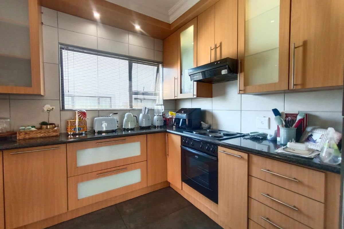 A functional kitchen featuring light wood cabinetry, dark granite countertops, a built-in oven, and a hob with an extractor fan.