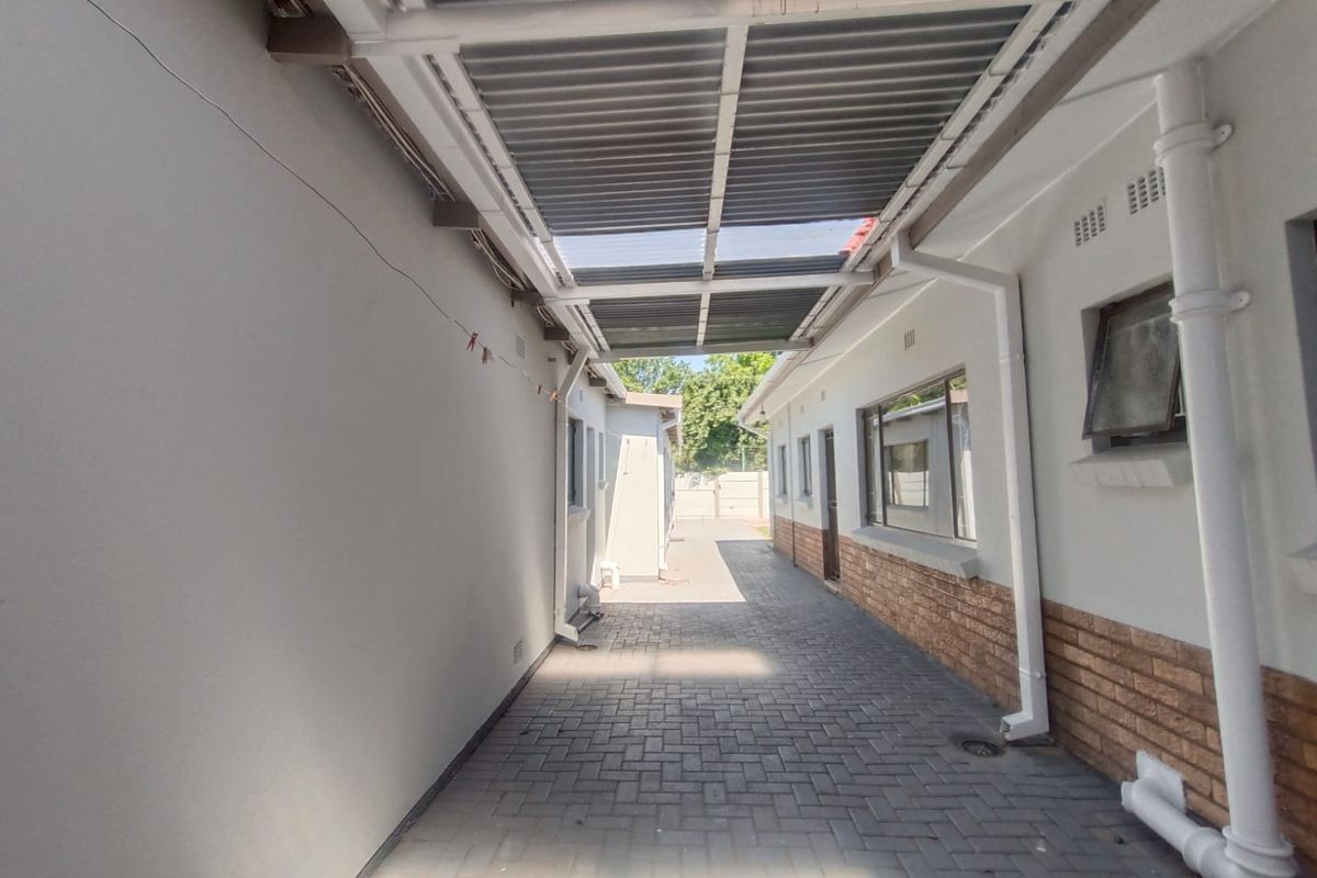 A paved side walkway featuring a covered corrugated metal roof structure, brick accents, and functional rainwater drainage systems.