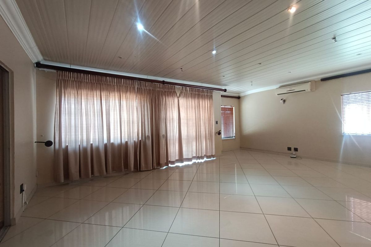 Spacious, light-filled living area featuring neutral tiled flooring, recessed downlighting, and a wall-mounted air conditioning unit.