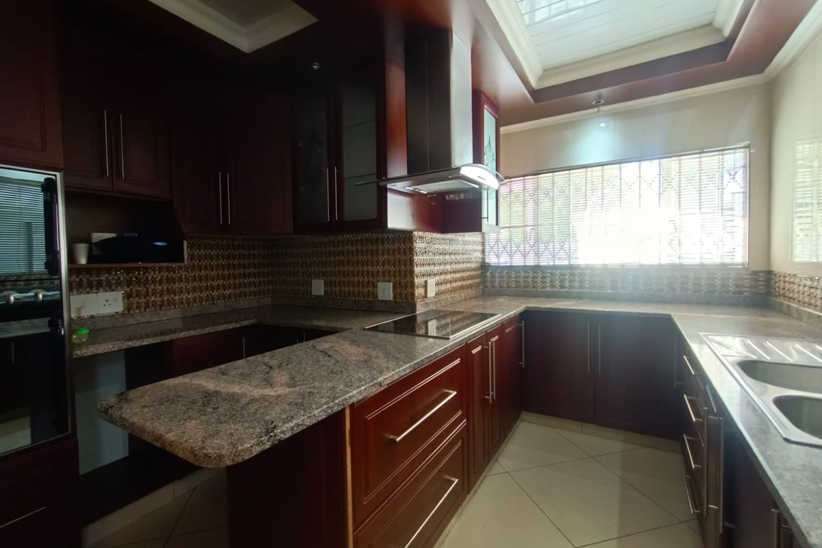 A spacious kitchen featuring dark wood cabinetry, granite countertops, built-in appliances, and tiled flooring with ample natural light.