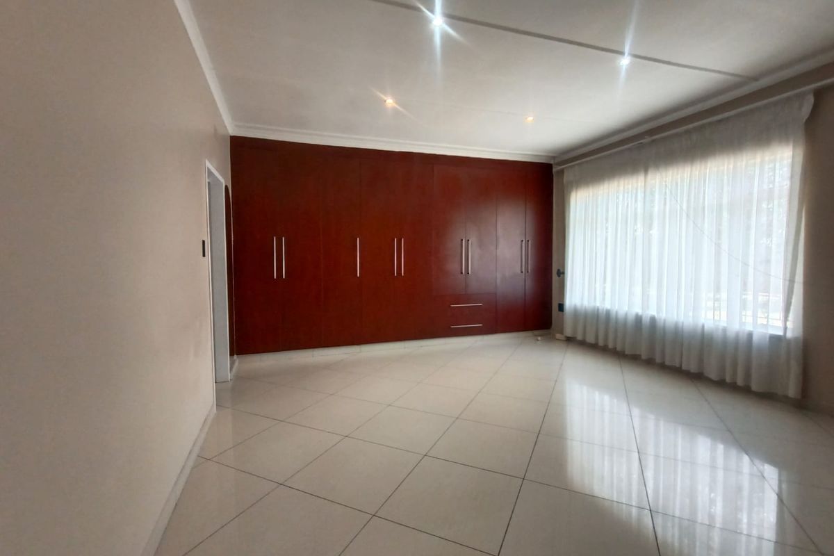 Spacious bedroom featuring large built-in wooden cupboards, neutral tiled flooring, and ample natural light through a large window.