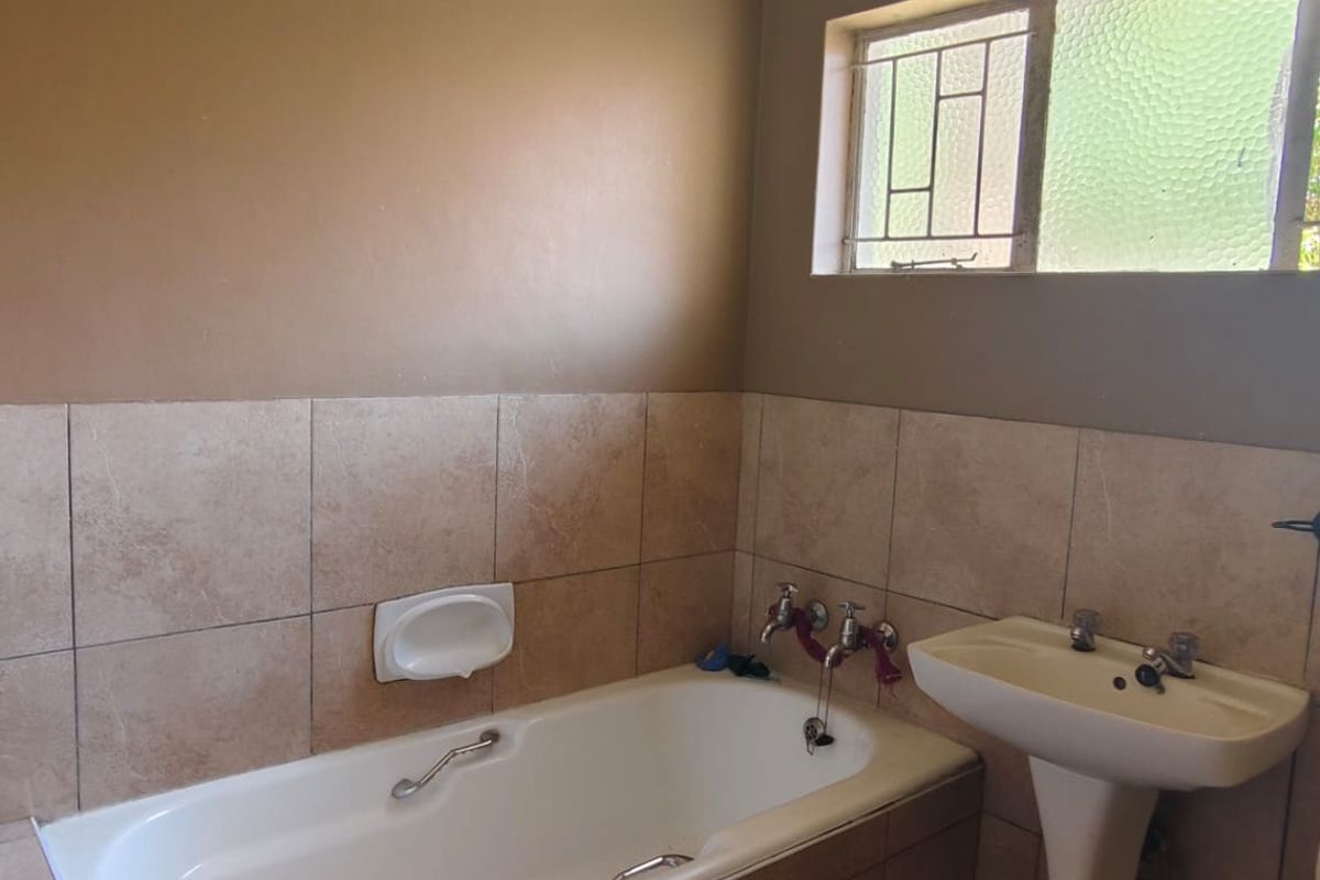 A functional bathroom featuring a built-in bathtub with tiled surround and a classic pedestal basin.