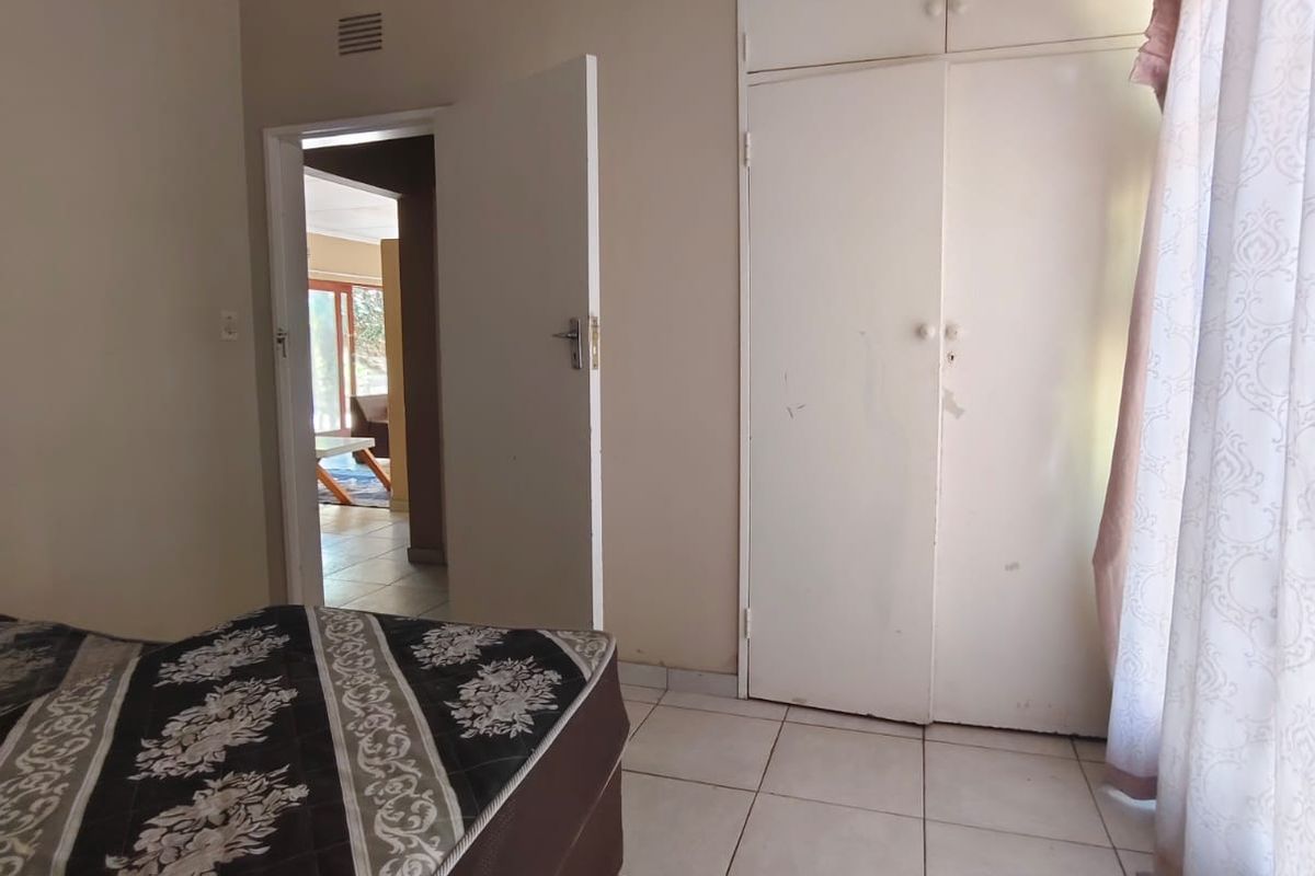 A bedroom featuring built-in cupboards, tiled flooring, and a doorway leading to an adjacent living area.