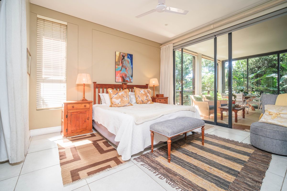 Spacious bedroom featuring large sliding glass doors that open onto a private patio, tiled flooring, and a ceiling fan.