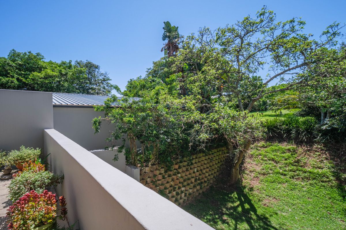 A view of the rear garden area featuring a retaining wall, mature trees, and a paved patio space.