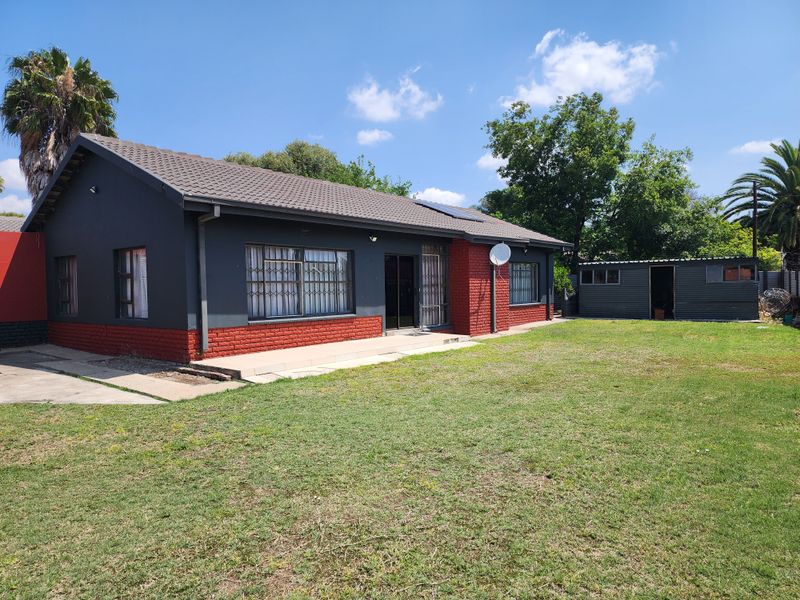 Rear view of a detached house featuring a painted brick facade, tiled roof, solar water heater, and a separate metal outbuilding set in a garden.