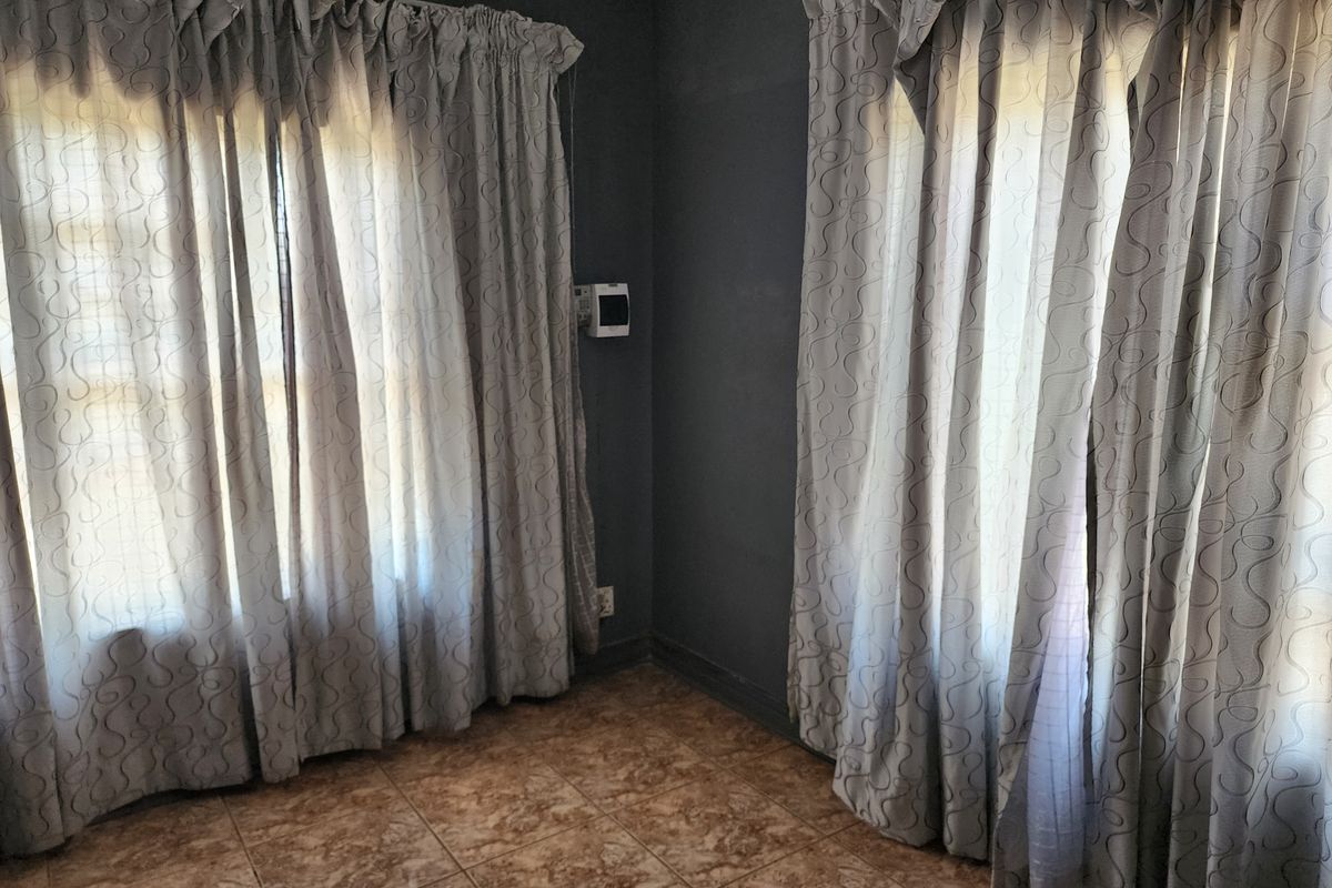 An empty living area featuring tiled flooring, dark grey walls, and dual window treatments.