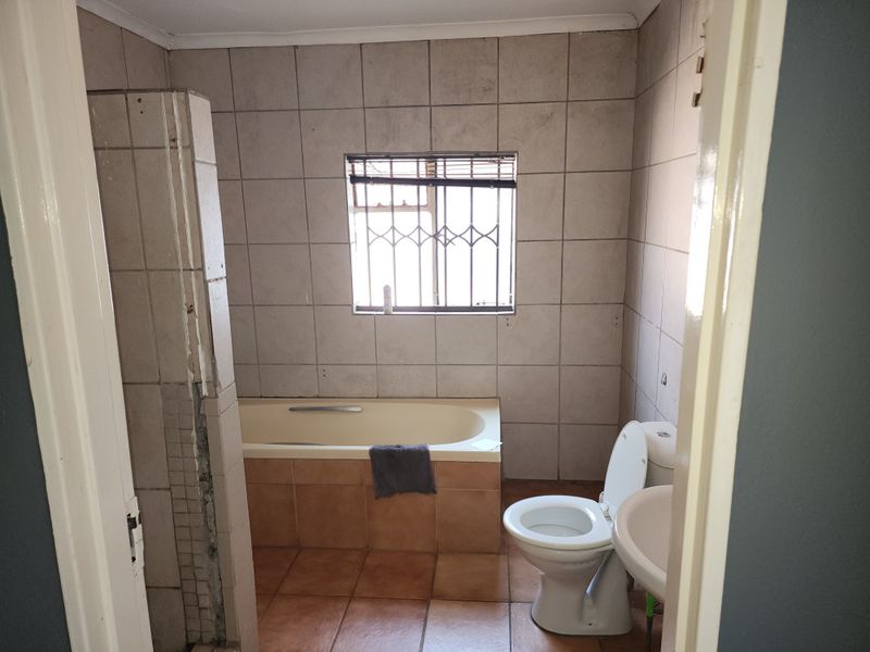 A functional bathroom featuring a built-in bathtub, pedestal sink, and toilet, finished with ceramic wall and floor tiles.
