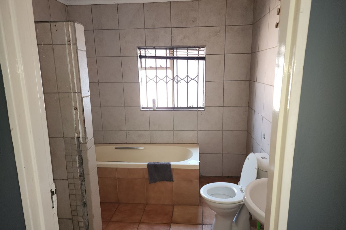 A functional bathroom featuring a built-in bathtub, pedestal sink, and toilet, finished with ceramic wall and floor tiles.