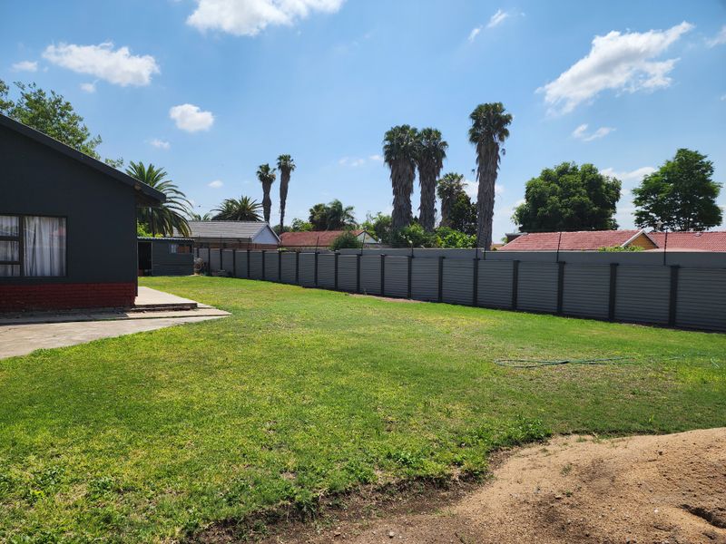 Spacious rear garden featuring a concrete patio area, well-maintained perimeter wall with security spikes, and an open lawn space.
