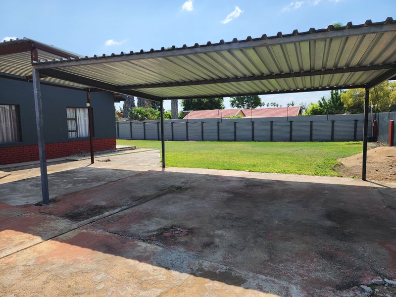 A covered outdoor patio area featuring a corrugated metal roof, steel support structure, and a concrete slab floor overlooking a spacious rear garden.