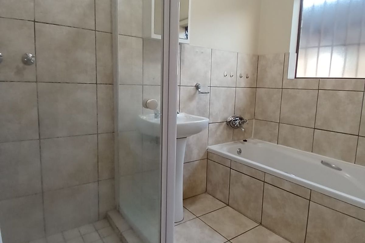 A functional bathroom featuring a separate glass-enclosed shower, a pedestal basin, and a built-in bathtub with neutral wall and floor tiling.