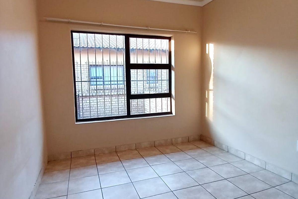 A vacant bedroom featuring neutral wall paint, tiled flooring, and a window fitted with security bars.