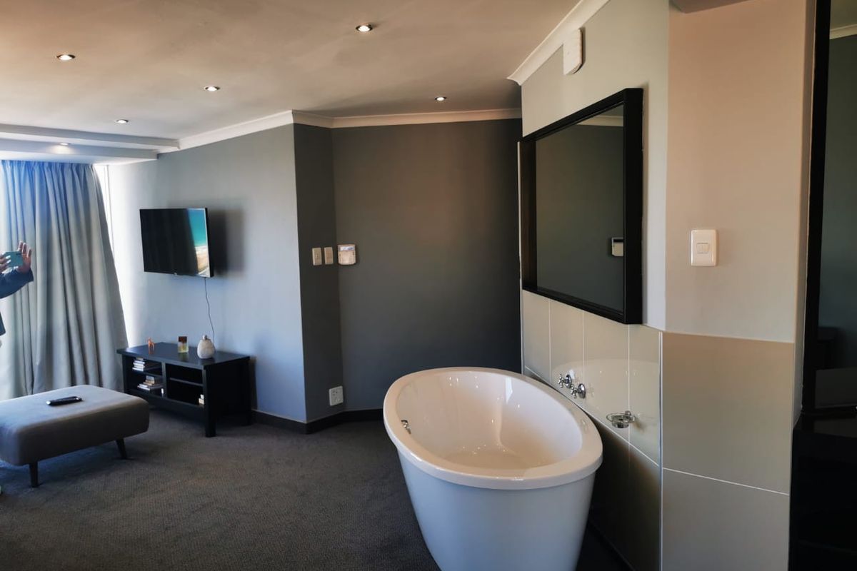 A modern bedroom suite featuring an open-plan layout with a freestanding bathtub integrated into the sleeping area, complemented by recessed ceiling lighting.