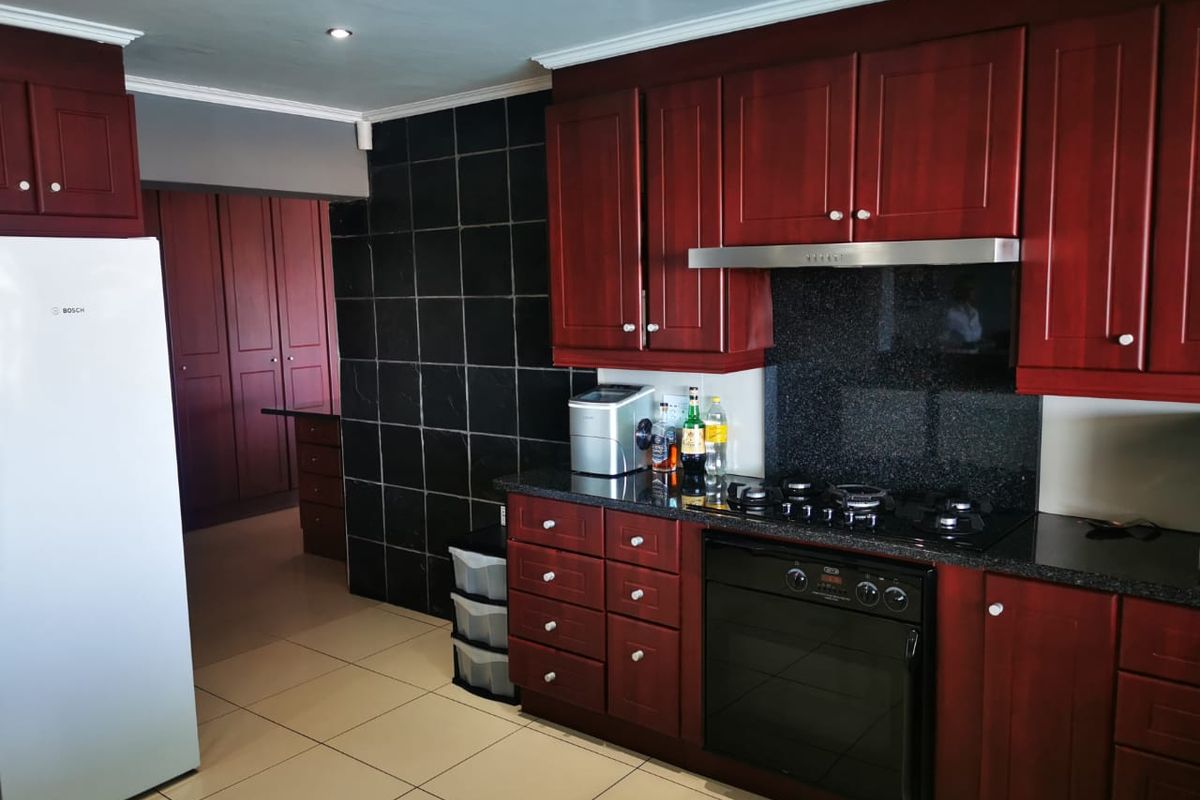 A functional kitchen featuring dark wood cabinetry, granite countertops, a built-in oven, gas hob, and a black tiled feature wall.