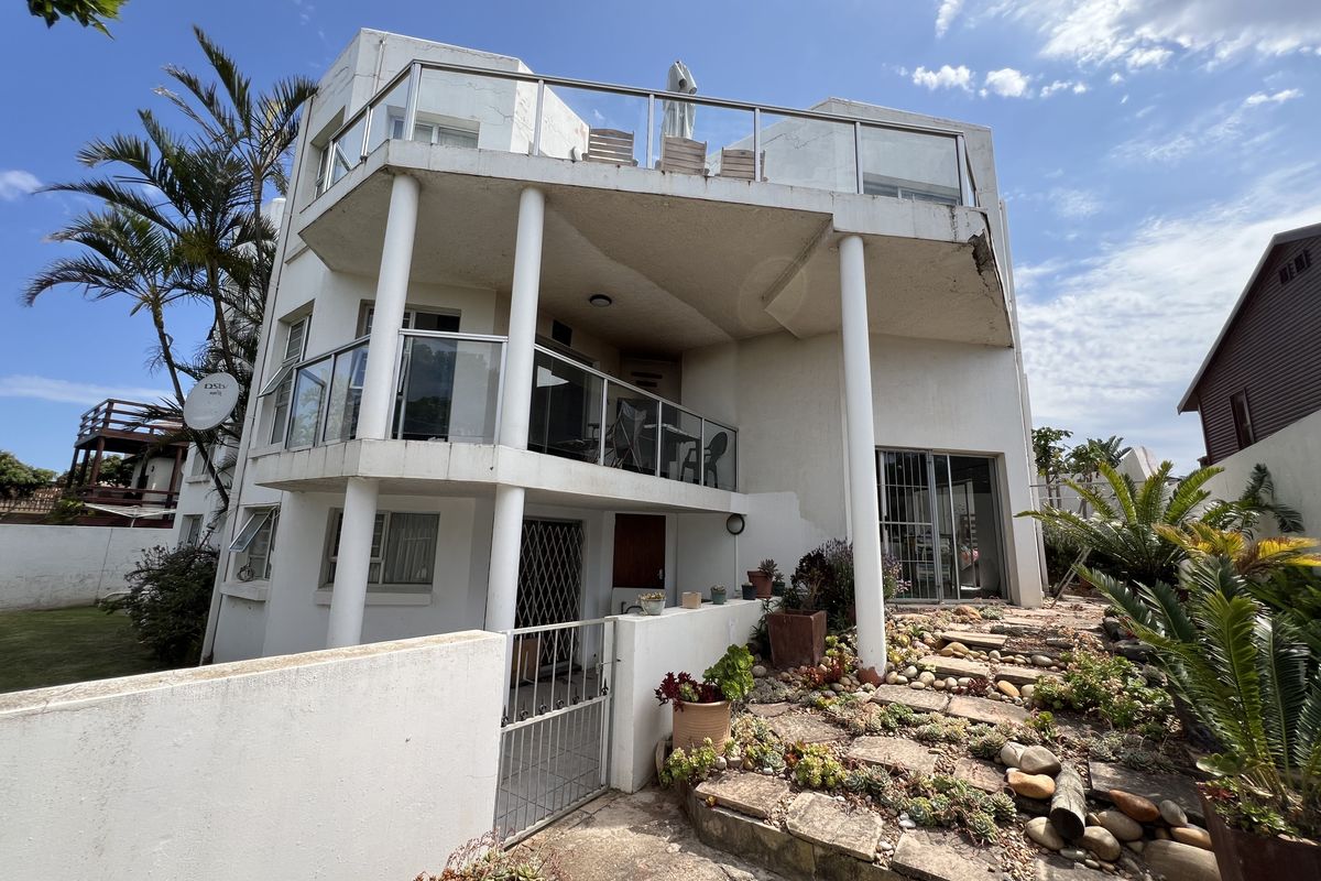 Multi-level residential exterior featuring tiered balconies with glass balustrades, structural columns, and a landscaped garden with stone pathway.