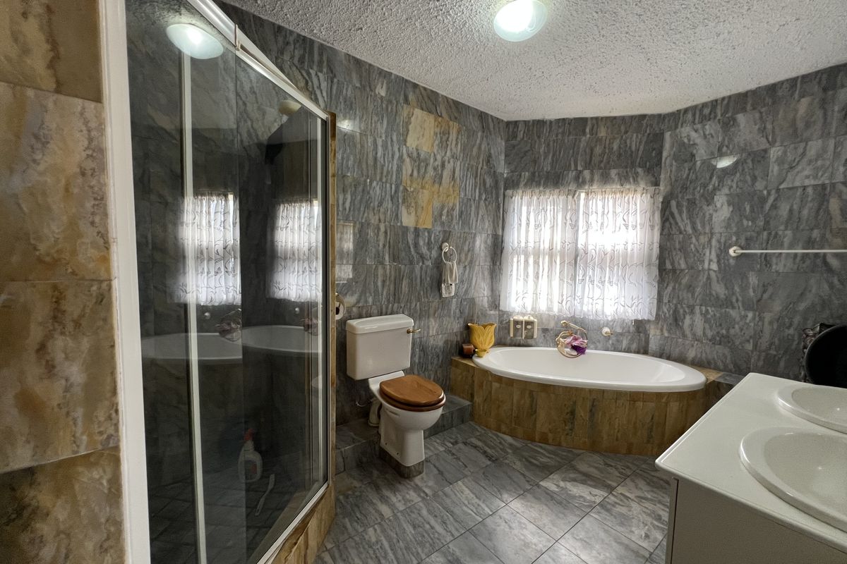 A spacious bathroom featuring a built-in oval bathtub, a separate glass-enclosed shower, a toilet, and a double vanity unit with marble-style wall tiling.
