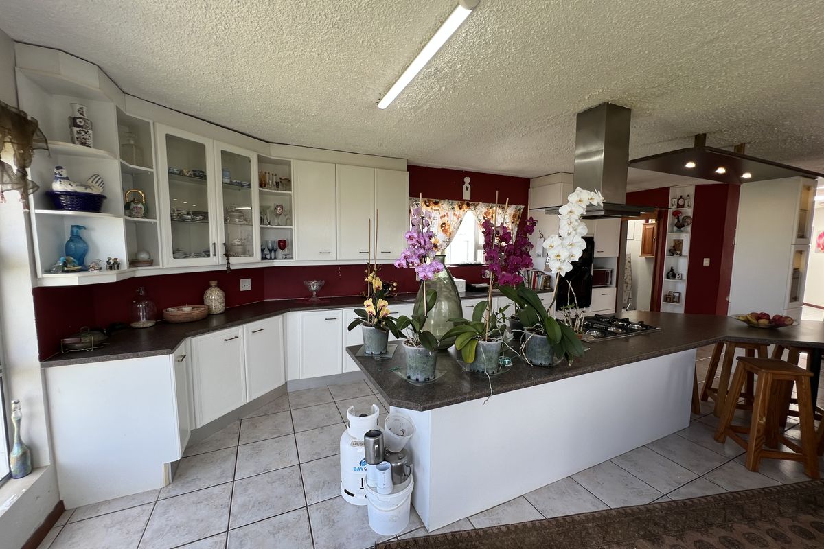 Spacious kitchen featuring white cabinetry, a central island with a built-in gas hob, stainless steel extractor fan, and tiled flooring.