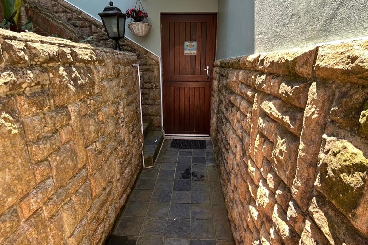 A narrow exterior walkway featuring stone-clad walls, tiled flooring, and a timber door with a protective canopy.