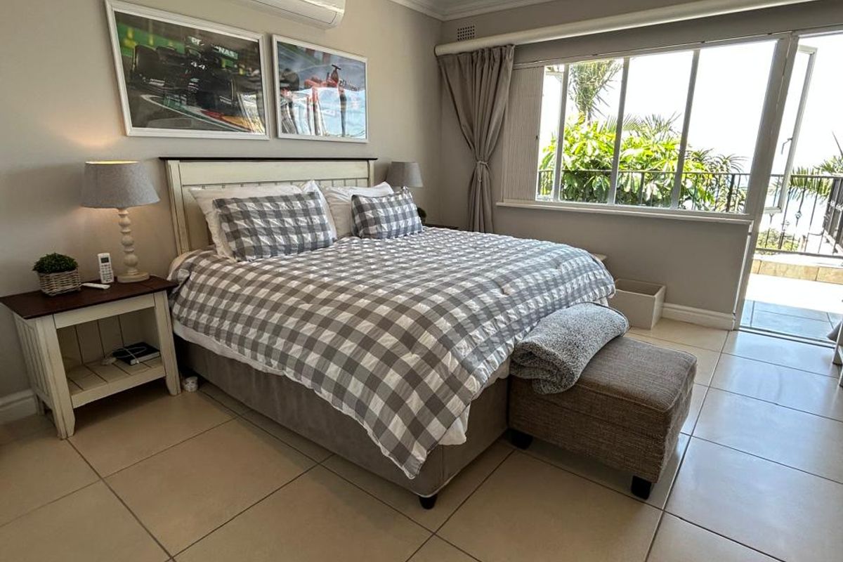 A well-maintained bedroom featuring tiled flooring, a ceiling fan, split-system air conditioning, and direct access to an outdoor balcony through sliding glass doors.