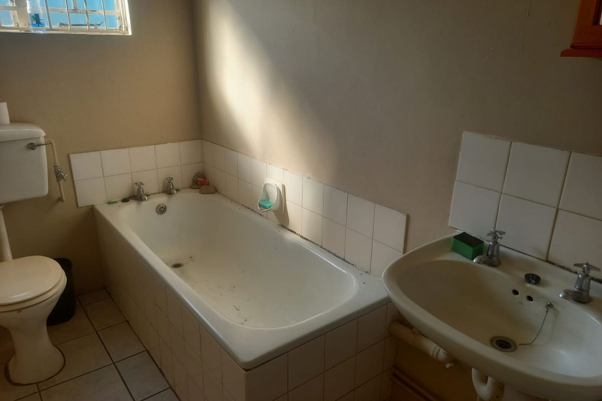 A functional bathroom featuring a standard bathtub, pedestal basin, and toilet with tiled splashbacks and natural light from a high-set window.