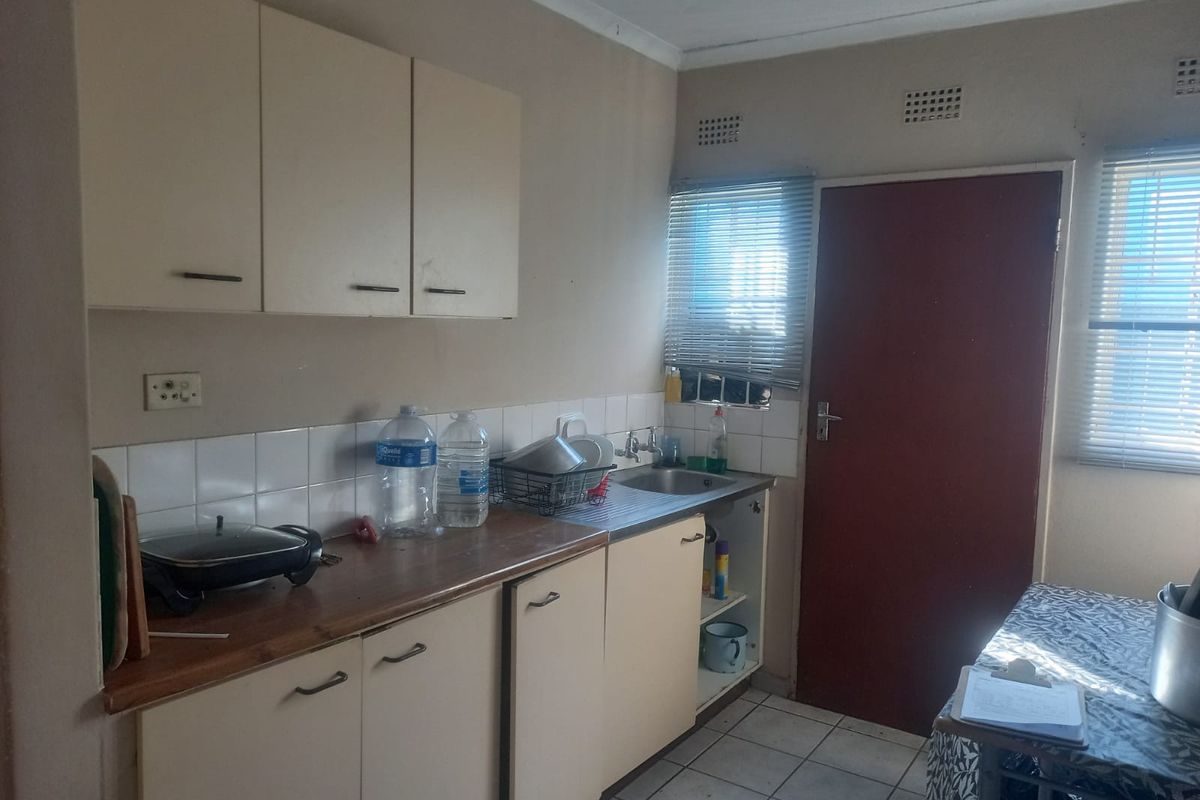 A functional kitchen area featuring built-in cabinetry, a stainless steel sink, tiled splashbacks, and direct access to an exterior door.