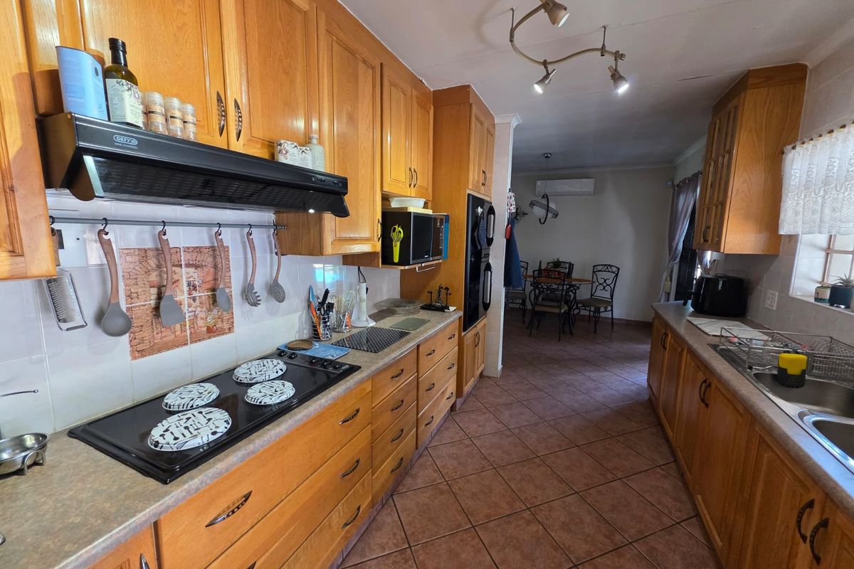 A functional kitchen featuring wooden cabinetry, a built-in oven, and a ceramic hob, leading into an adjacent dining area.