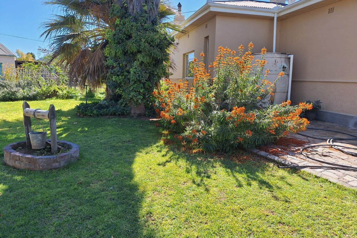 A rear garden area featuring a lawn, established landscaping, a brick-paved patio section, and a decorative stone well feature.