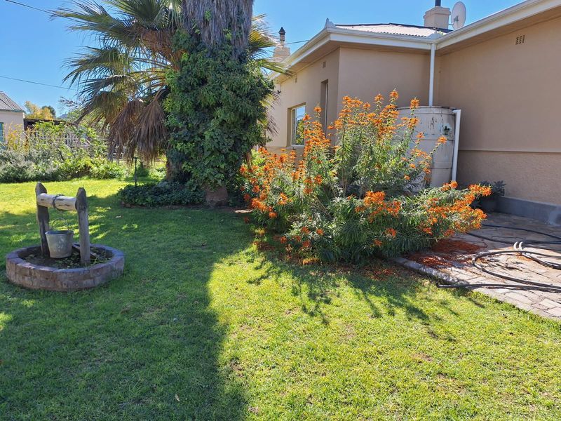 A rear garden area featuring a lawn, established landscaping, a brick-paved patio section, and a decorative stone well feature.