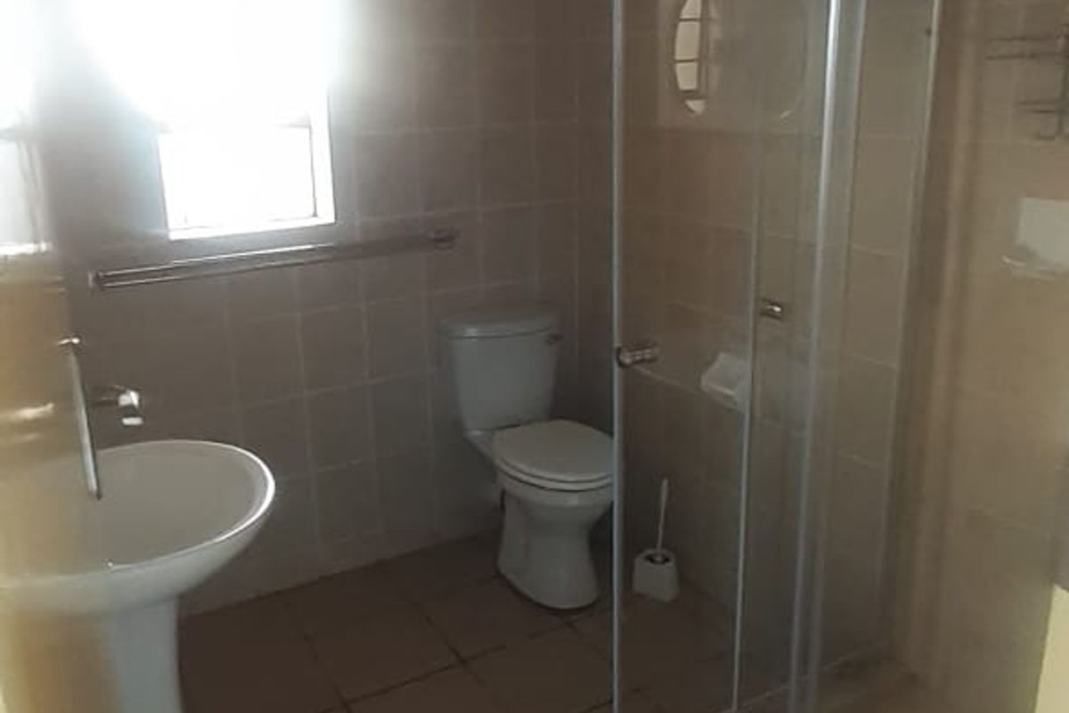 A functional bathroom featuring a pedestal basin, a toilet, and a glass-enclosed shower stall with tiled flooring and walls.