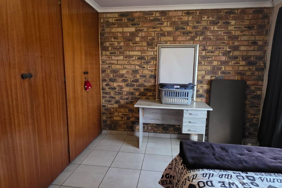 A bedroom featuring a rustic face-brick feature wall, built-in wooden cupboards, and tiled flooring.