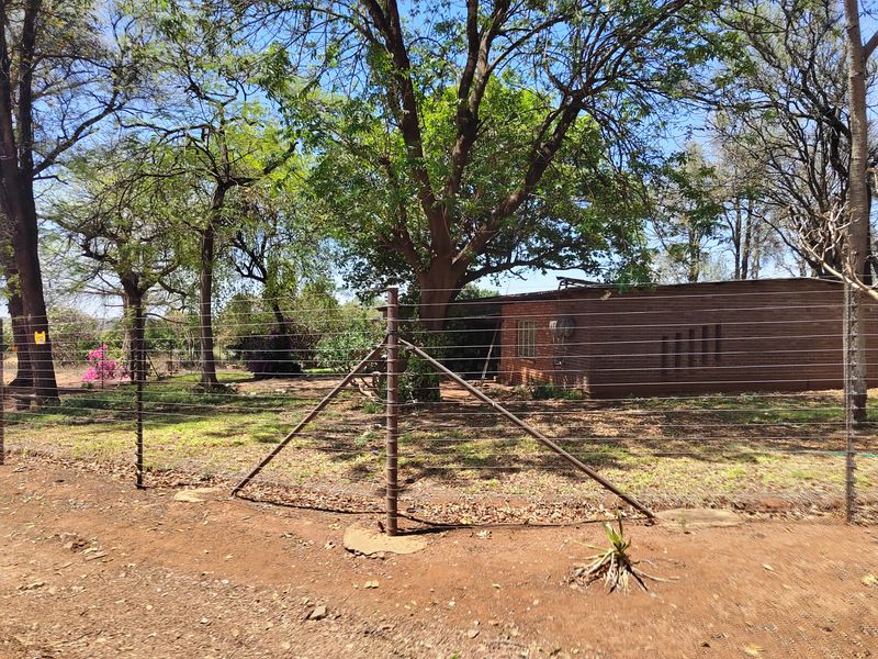 Front view of a farm property featuring a brick exterior, mature trees, and perimeter electric fencing.