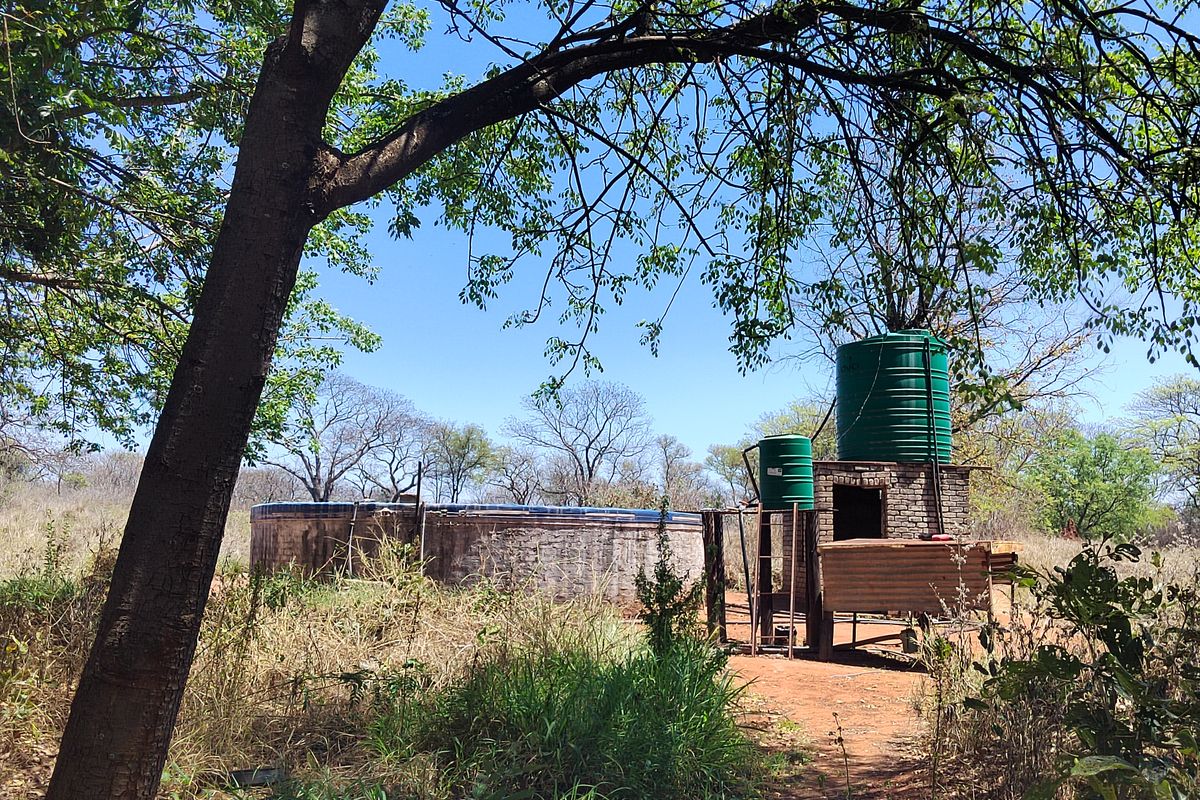 Outdoor utility area featuring a circular reservoir, brick pump house, and elevated water storage tanks on a farm property.