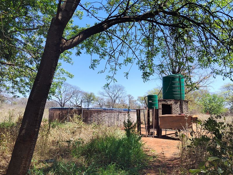 Outdoor utility area featuring a circular reservoir, brick pump house, and elevated water storage tanks on a farm property.