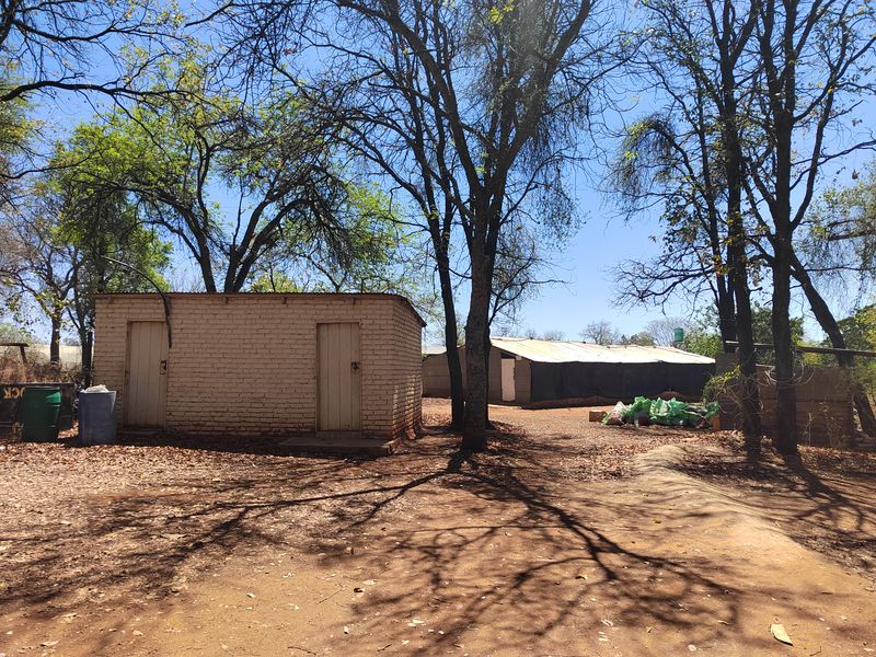 A view of the farm property showing a brick outbuilding and a secondary structure with a corrugated metal roof set within a wooded area.