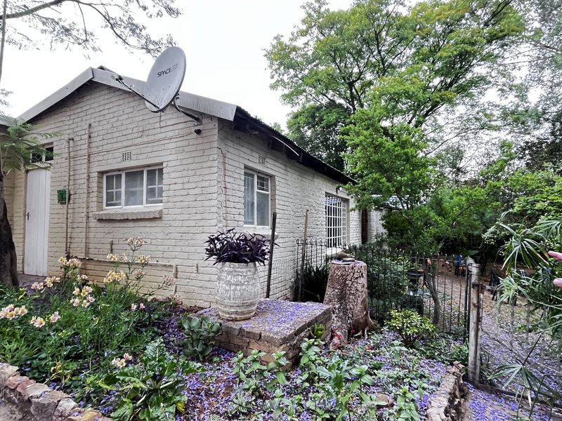 Exterior view of a brick-built small holding dwelling featuring a satellite dish, metal security gate, and established garden surroundings.