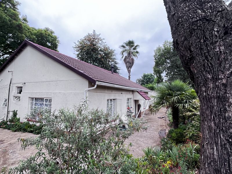 Side view of a residential dwelling featuring a tiled roof, concrete pathways, and established garden surroundings on a small holding property.