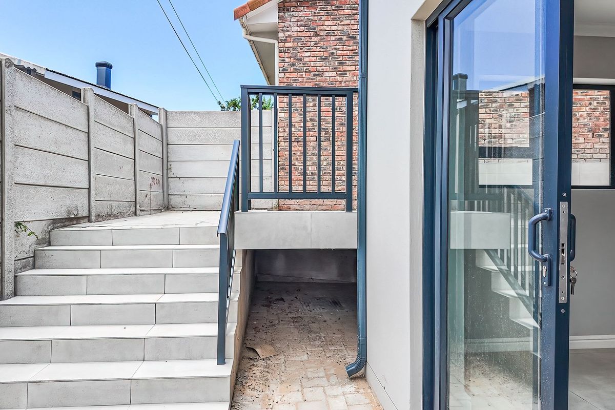 Rear exterior view featuring a tiled staircase with metal balustrade, leading to a sliding glass door entrance with brick and rendered wall finishes.