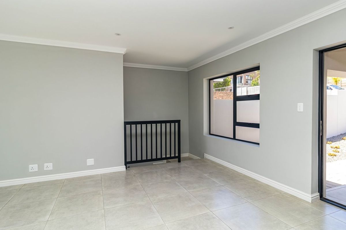 A bright, empty living area featuring neutral tiled flooring, modern black-framed windows, and a sliding door providing access to the outdoor space.