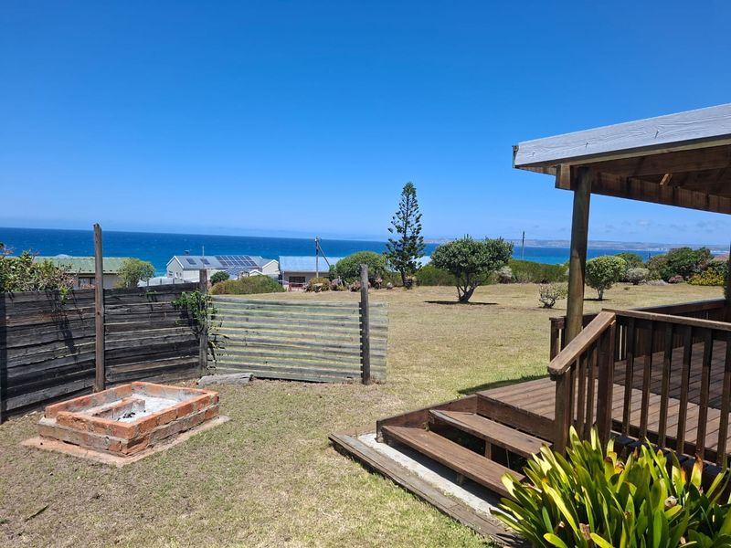 Rear garden area featuring a timber deck, stairs, and a brick fire pit, offering an open outdoor space with coastal views.